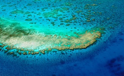 An aerial photo of turquoise and darker blue water around an area of the Great Barrier Reef. 